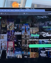 A laptop screen displays a web page featuring a mix of movie and TV show covers, highlighting popular titles and a Hulu and Disney+ bundle promotion. There are visible icons and images of films and shows alongside promotional text offering entertainment and live sports.