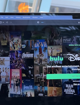A laptop screen displays a web page featuring a mix of movie and TV show covers, highlighting popular titles and a Hulu and Disney+ bundle promotion. There are visible icons and images of films and shows alongside promotional text offering entertainment and live sports.