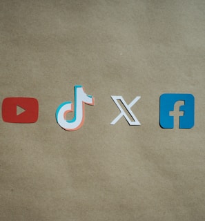 Four social media platform logos are arranged on a brown background. From left to right, the logos are for YouTube in red, TikTok in a combination of red, blue, and white, X in white, and Facebook in blue.